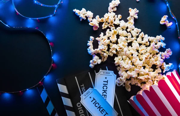 Billete, palomitas de maíz, tira de película y aplausos, películas y concepto de entretenimiento sobre fondo negro con luz de neón azul, flatlay —  Fotos de Stock