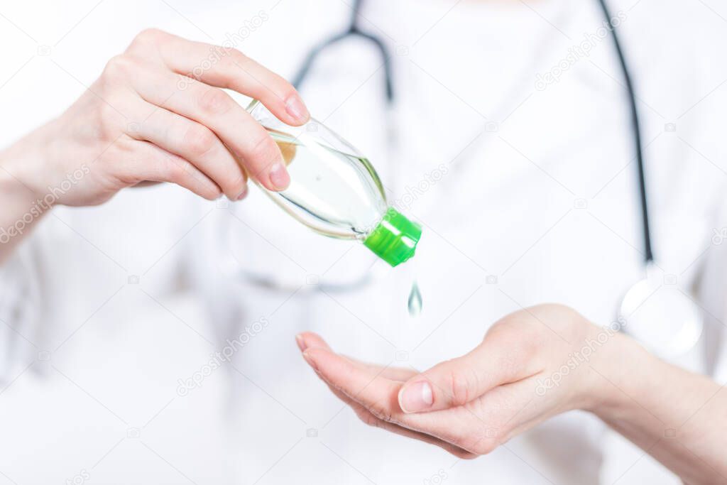 Coronavirus COVI 19 . Young smiling woman brunette doctor in glasses and medical white coat with stethoscope squeezing out a vial with clear liquid in palm