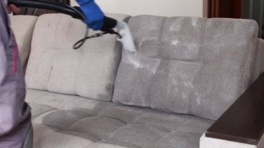 Temizlik servisi. Eldivenli ve elektrikli süpürgeli adam. Profesyonel ekipmanlı temiz kanepe.