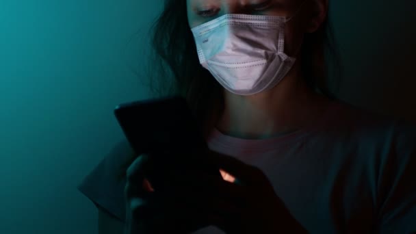 Una mujer con una máscara médica en cuarentena, período de aislamiento. utiliza un teléfono inteligente, envía un mensaje — Vídeos de Stock