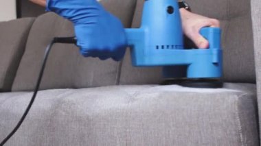Temizlik servisi. Eldivenli ve elektrikli süpürgeli adam. Profesyonel ekipmanlı temiz kanepe.