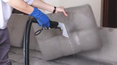 Temizlik servisi. Eldivenli ve elektrikli süpürgeli adam. Profesyonel ekipmanlı temiz kanepe.