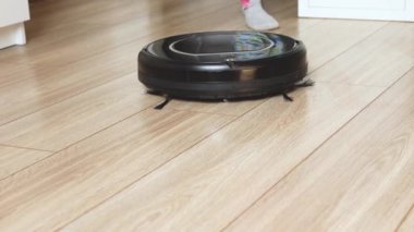 Küçük çocuk elektrik süpürgesinin düğmesine basıyor. Yerdeki kendi kendine hareket eden robotik vakumun detaylı görüntüsü.