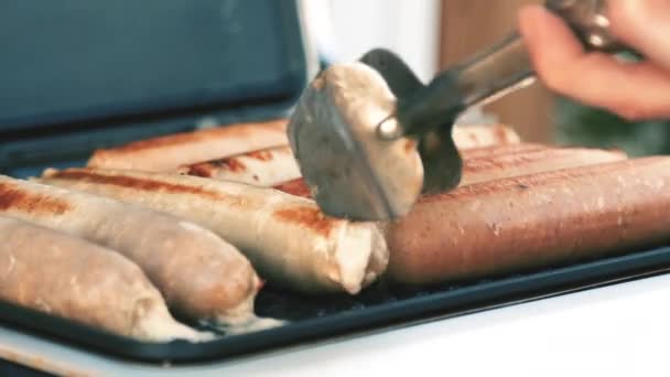 Churrasco com salsichas de fogo na grelha em um piquenique ao ar livre. close-up de mãos femininas com pinças — Vídeo de Stock