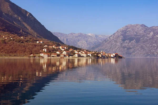 Las montañas y la pequeña ciudad de Prcanj se reflejan en el agua de Kotor Bay en un día soleado de invierno. Montenegro —  Fotos de Stock