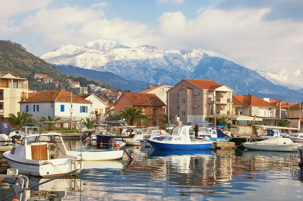 Rybářské lodě v přístavu na pozadí zasněžených horských vrcholků. Černá Hora, Bay of Kotor. Pohled na Marina Kalimanj v městě Tivat a zasněžené hory Lovcen — Stock fotografie