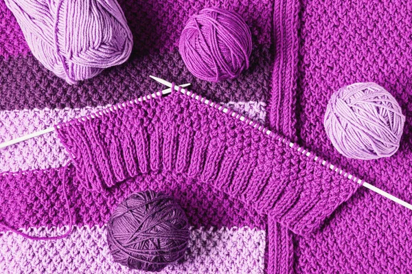 Balls of wool  and unfinished knitting in violet tones, flat lay