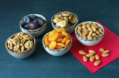 Çeşitli Kuruyemiş (kayısı, incir, tarihler) ve koyu arka plan üzerinde küçük kase fındık (ceviz ve badem)