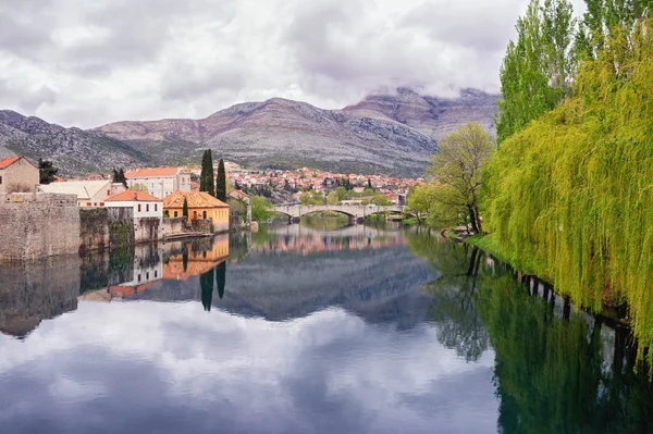 Nublado día de primavera. Las nubes, las montañas, los árboles verdes y la ciudad se reflejan en el agua del río. Bosnia y Herzegovina. Vista del río Trebisnjica y el casco antiguo de Trebinje —  Fotos de Stock