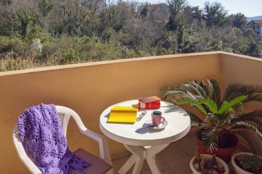 Evde vakit geçirmek. Kitaplar ve bir fincan kahve beyaz masada güneşli bir bahar gününde küçük balkonda.