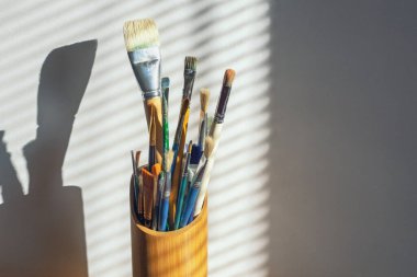 Duvara karşı resim yapmak için farklı türde fırçalar. Jaluziyle pencereden güneş ışığı geliyor. Boşluğu kopyala