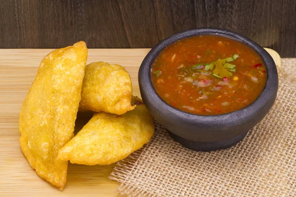 Colombian empanada with spicy sauce on wooden background