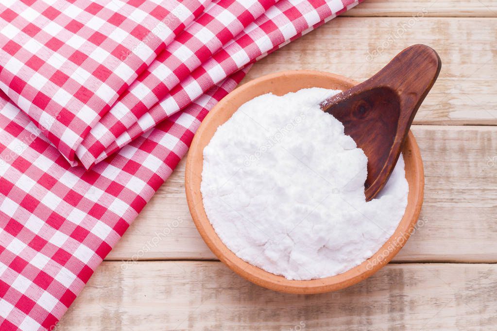 Baking soda in a bowl with spoon and dough cloth on wooden background