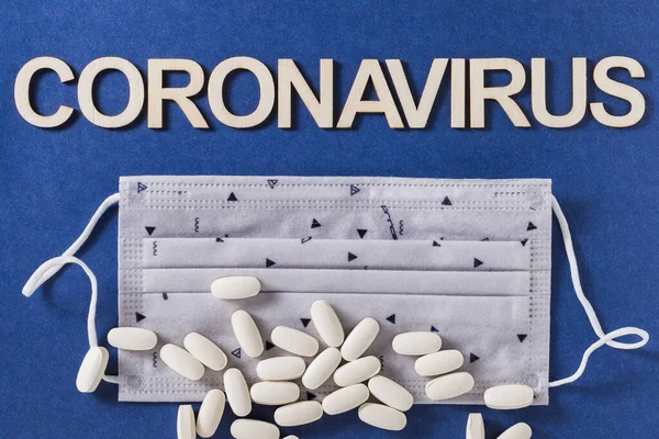 Coronavirus Wort Mit Holzbuchstaben Gesichtsschutzmaske Und Komprimierten Medikamententabletten Auf Blauem — Stockfoto