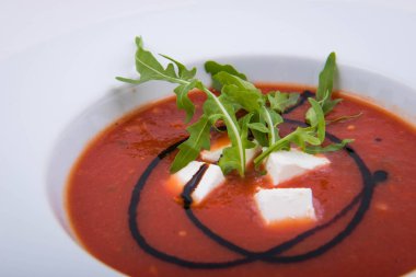 Roka ve mozzarellalı beyaz tabakta domates çorbası