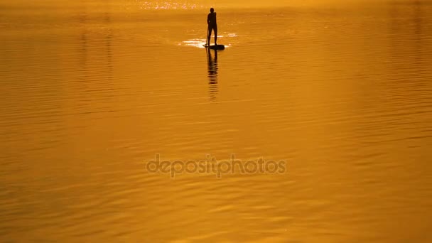 SUP surf στο φόντο ηλιοβασίλεμα ουρανό. Ακτίνες του ήλιου — Αρχείο Βίντεο