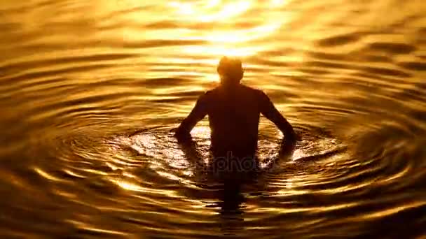 O homem derrama-se com água do mar ao pôr-do-sol — Vídeo de Stock