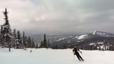 Aktif kayakçı çam ormanlarında inanılmaz bir kayak yamacında geriye doğru hareket ediyor. Dağlık bölgede güneşli bir günde manzaranın tadını çıkarıyorum.