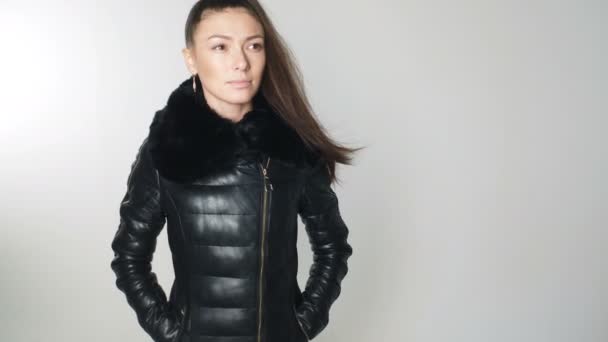 Woman with long hair in wind in down jacket posing in studio on white background — Stock Video