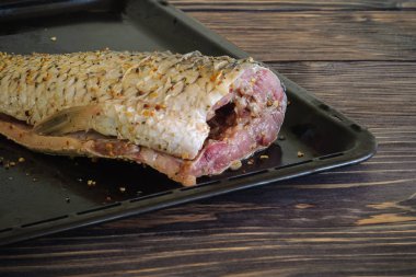 Ahşap bir arka planda metal bir fırın tepsisine yakın çekim yapmak için baharatlarla rendelenmiş büyük çiğ başsız sazan. açılı kenar görünüm