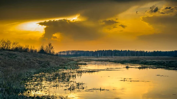 Dramatische herfst oranje zonsondergang weerspiegeld op het wateroppervlak in een smalle rivier met moerassige grasoevers — Stockfoto