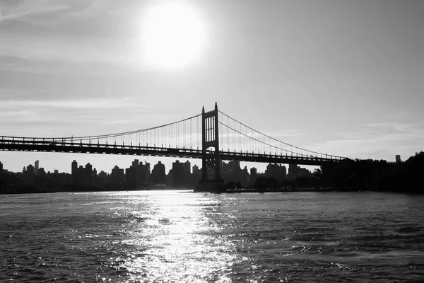 Silhouette of Triborough bridge over reflective river and buildings in black and white style, New York — Stock Photo, Image