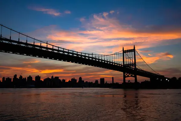 Ponte di Triborough sul fiume e gli edifici in silhouette e cielo al tramonto — Foto Stock