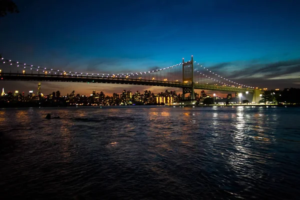 Triborough-Brücke über den spiegelnden Fluss und Gebäude bei Nacht, New York — Stockfoto