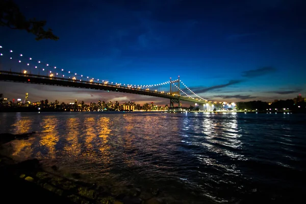 Triboroughen bro över reflekterande floden och byggnader på natten, New York — Stockfoto