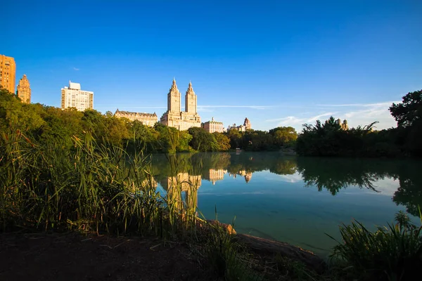 Los edificios se reflejan en el lago en Central Park con cielo azul, Nueva York — Foto de Stock