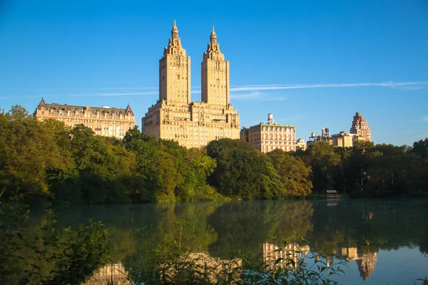 Edificios en Manhattan reflexionan sobre el lago en Central Park con cielo azul, Nueva York — Foto de Stock