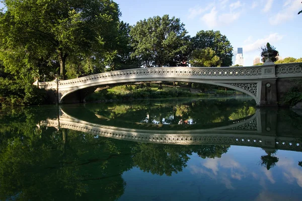 Podul Bow se reflectă pe lacul din Central Park în lumina dimineții și clădirile din Manhattan — Fotografie, imagine de stoc