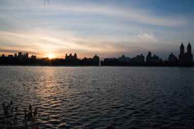 Binalar ve karanlık göl üzerinde bulanık günbatımı