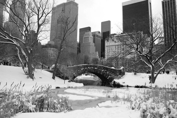 Buildings and Gapstow bridge over the icy pond and snow at Central Park in black and white style