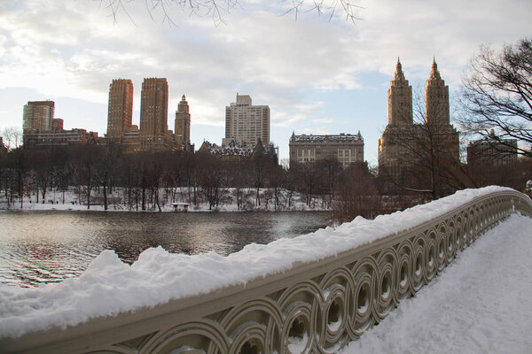 Bow bridge's covered by snow and buildings in Manhattan