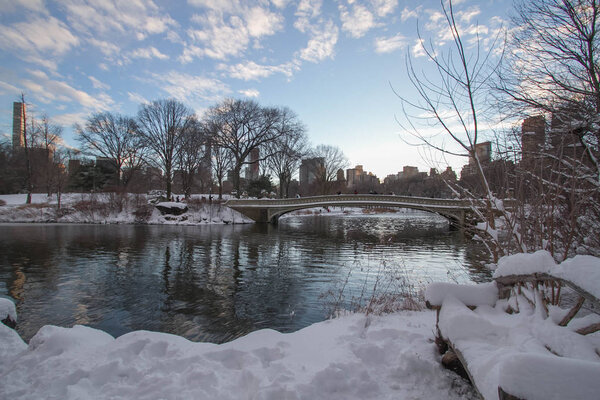 Bow bridge over the reflective lake with snow before sunset, Central Park, New York