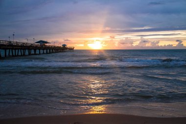 Plaj ve İskele üzerinde gündoğumu yansıtır