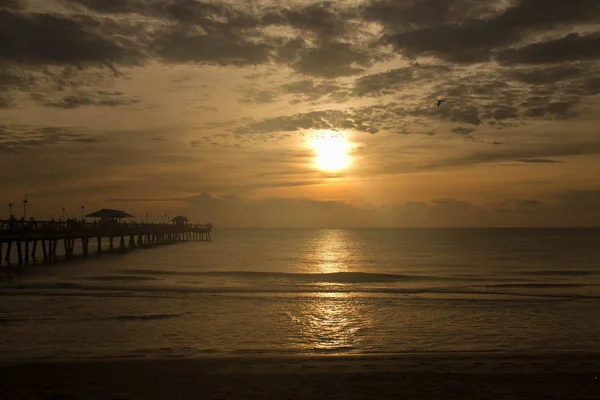 Nascer do sol reflete sobre o oceano escuro e cais — Fotografia de Stock