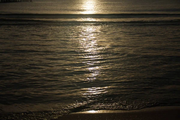Sunlight reflects on dark waving sea water on beach