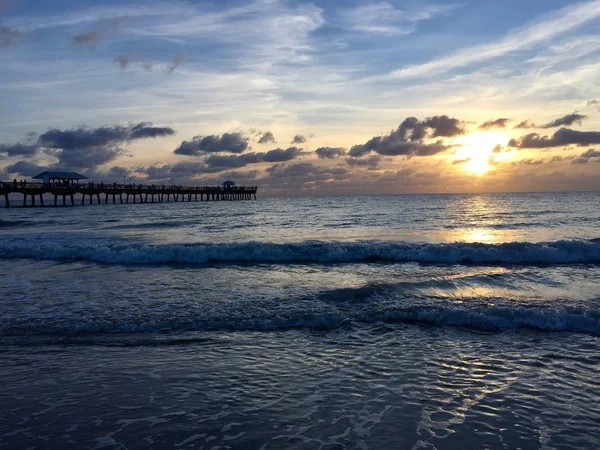 Nascer do sol atrás da nuvem na praia e no cais — Fotografia de Stock