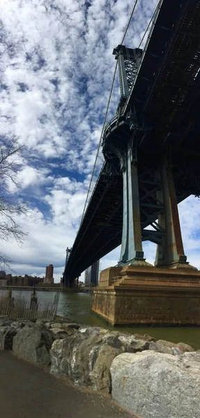 Pont de Manhattan sur la rivière et les rochers au Brooklyn bridge park avec ciel nuageux — Photo