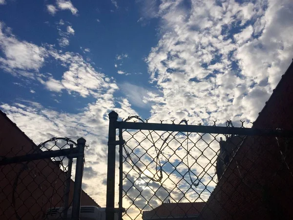 Wolkenverhangener Blauer Himmel Hinter Silhouettenzaun Und Gebäude — Stockfoto