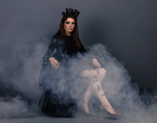 Bugg drottning kvinna med krona bär svart klänning med klänning sitter i rök — Stockfoto