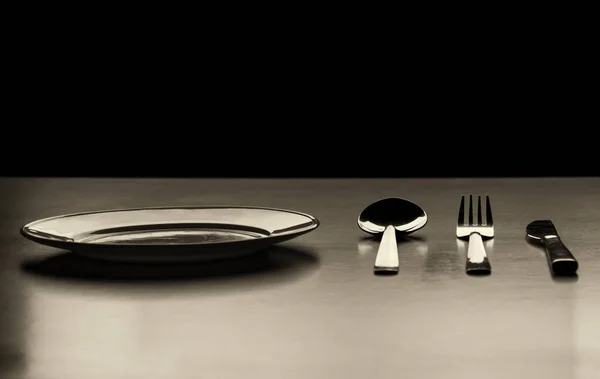 Lege plaat met lepel, mes en vork op een zwarte achtergrond — Stockfoto