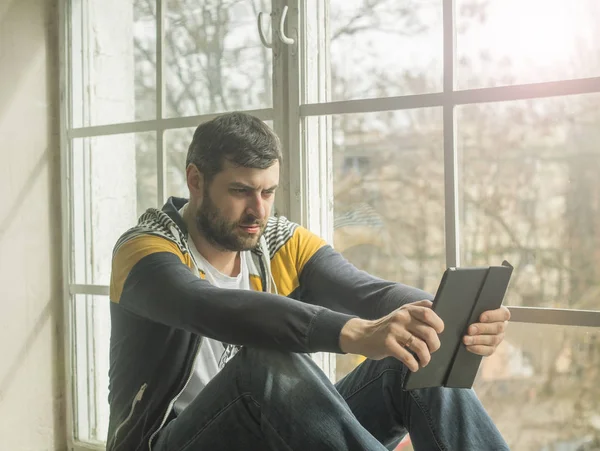 Hombre usando una tableta digital mientras está sentado en el alféizar de la ventana — Foto de Stock