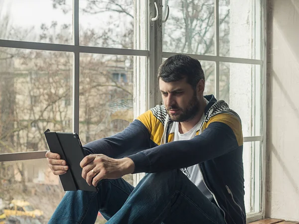 Человек с помощью цифрового планшета, сидя на подоконнике — стоковое фото