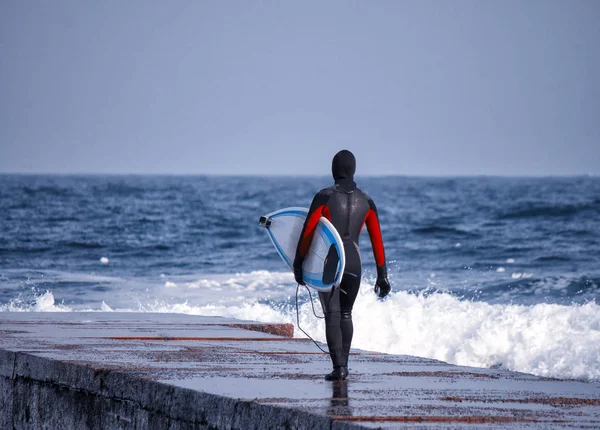 Surfista entra no oceano vestindo um fato de mergulho no inverno — Fotografia de Stock