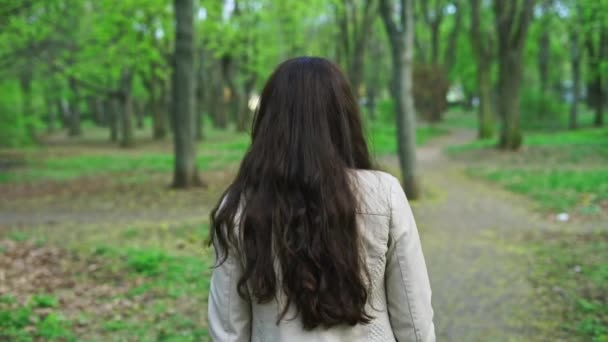 Glad ung flicka promenader och vrida runt med ett leende i parken — Stockvideo