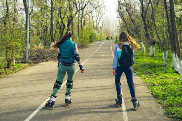 Dos chicas en patines se pasean por la carretera una al lado de la otra —  Fotos de Stock