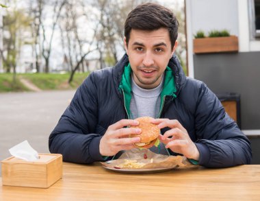 Genç adam sokak gıda kafede hamburger yeme portresi